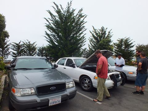 2003 Ford Crown Victoria - Photograph of a group standing by parked sedans with one hood up, not a technical document.
