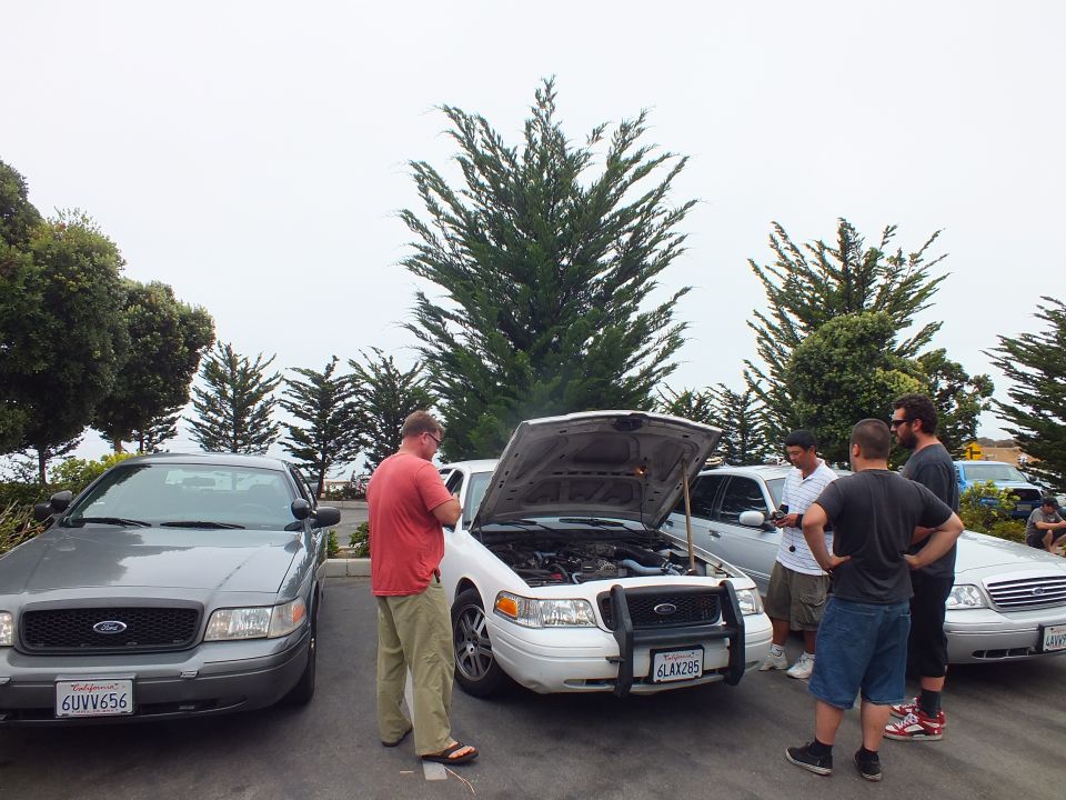 Men around a white sedan with the engine bay exposed