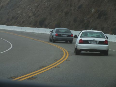 2003 Ford Crown Victoria - Photograph of two sedans driving on a curving mountain highway, not a technical document.