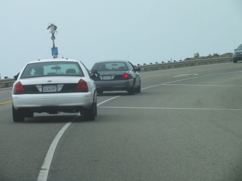 2003 Ford Crown Victoria - Photo of a white Ford Crown Victoria following a dark sedan along a foggy coastal highway, not a technical document.