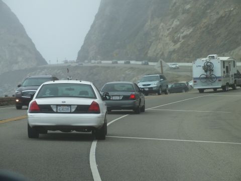 2003 Ford Crown Victoria - Photo of a white Crown Victoria in traffic behind several cars and a bicycle-laden RV on a foggy mountain highway, not a document.