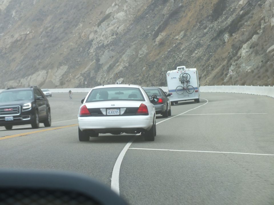 White Crown Victoria following an RV around a curve on a mountain highway