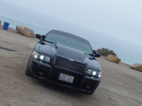 2003 Ford Crown Victoria - Photo of a black customized Crown Victoria with push bumper and EVIL VIC plate parked at a foggy coastal overlook, not a document.
