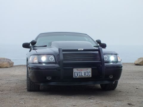 2003 Ford Crown Victoria - Photo of a black customized Crown Victoria front view at a foggy coastal pullout, not a document.