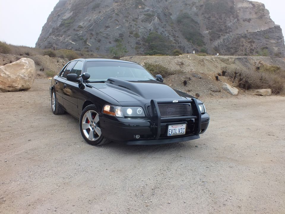 Black 'EVIL VIC' Crown Victoria three-quarter view before a rocky hill