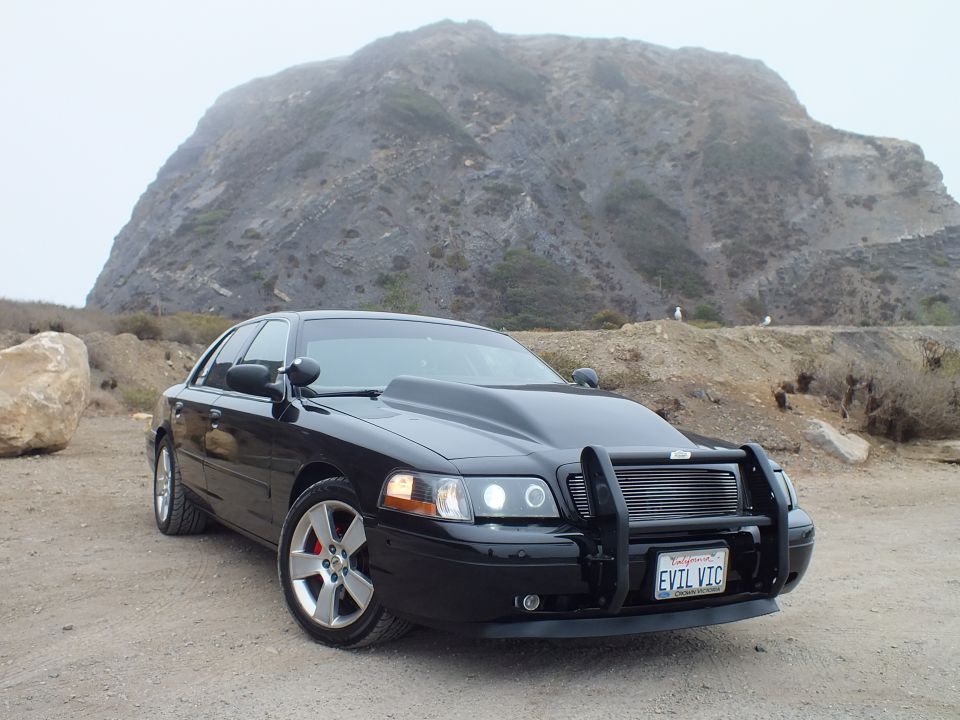 Black 'EVIL VIC' Crown Victoria side-front view with mountain backdrop