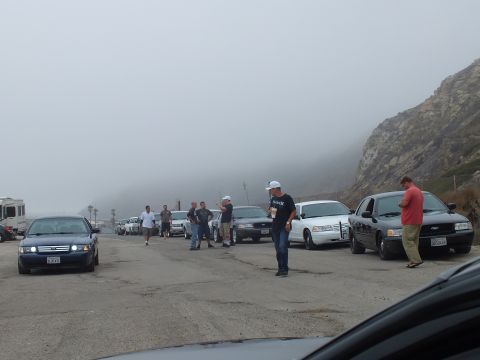 2003 Ford Crown Victoria - Photo of a car-club meet with people and parked Crown Victorias at a foggy coastal pullout, not a document.