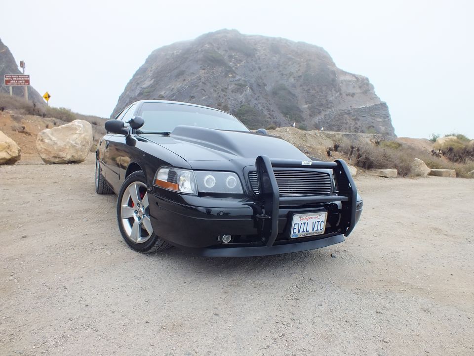 Front three-quarter view of a black sedan with grille guard and red brake calipers near a rock outcrop