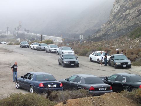 2003 Ford Crown Victoria - Photograph of a car meetup with parked sedans and a pickup at a foggy coastal lot; not a technical document.
