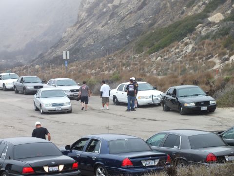 2003 Ford Crown Victoria - Photograph of attendees walking among parked sedans at a coastal car meetup; not a technical document.