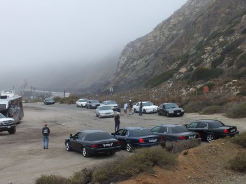 2003 Ford Crown Victoria - Photograph of sedans parked at a foggy coastal lot with an RV and people; not a technical document.