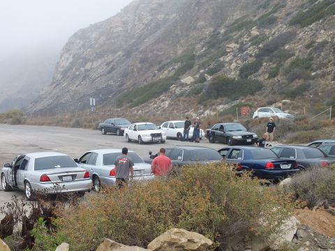 2003 Ford Crown Victoria - Photograph of attendees standing among parked sedans at a foggy coastal car meetup; not a technical document.