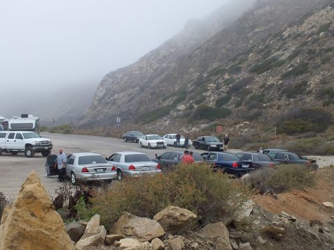 2003 Ford Crown Victoria - Photograph of a car meetup with parked sedans, a pickup, an RV, and people at a foggy coastal lot; not a technical document.