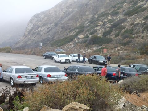 2003 Ford Crown Victoria - Photograph of attendees and parked sedans at a hazy coastal lot car meetup; not a technical document.