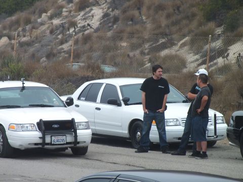 2003 Ford Crown Victoria - Photograph of men talking beside white and black sedans at a coastal parking lot; not a technical document.