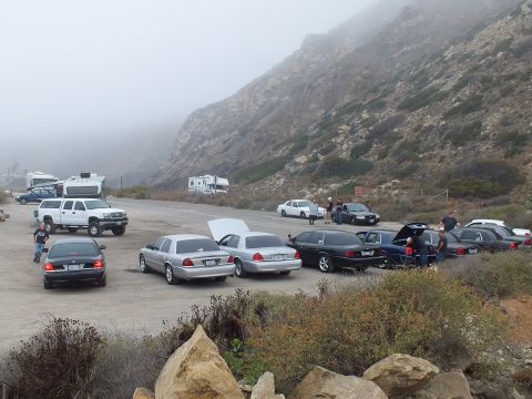 2003 Ford Crown Victoria - Sedans and SUVs parked across a gravel lot with an RV and pickup nearby beneath foggy mountains.