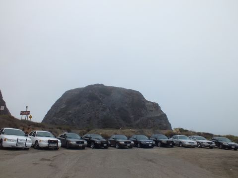 2003 Ford Crown Victoria - row of parked sedans sits before a large rock formation, with a red roadside sign visible at left.