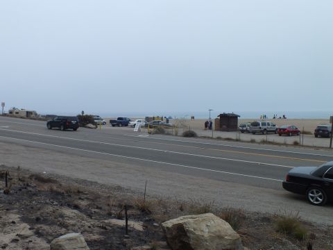 2003 Ford Crown Victoria - Vehicles parked and driving along a two-lane coastal highway beside a broad sandy beach shrouded in gray fog.