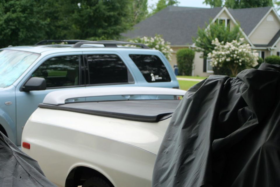 Side view of a white pickup truck with a tonneau cover, parked next to a blue SUV