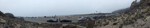 2003 Ford Crown Victoria - panoramic view of sedans parked along a foggy coastal highway, framed by rocky bluffs and a sandy beach.