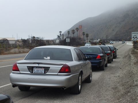 2003 Ford Crown Victoria - rear of a silver Mercury Marauder is parked on a highway shoulder ahead of other dark sedans.