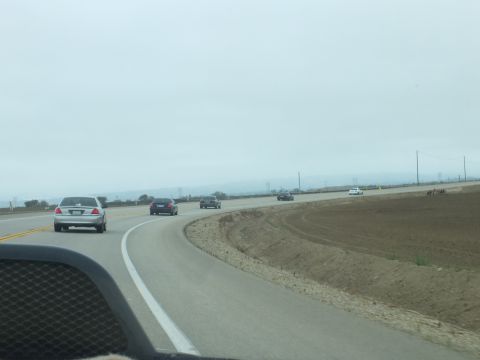 2003 Ford Crown Victoria - Seen through a windshield, several sedans travel a curving rural highway beside open plowed fields.