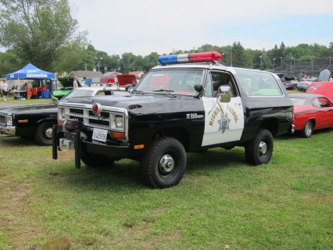 1991 Ford LTD Crown Victoria - black-and-white Dodge Ramcharger marked Highway Patrol with roof lightbar, on grass at a car show among classic cars.