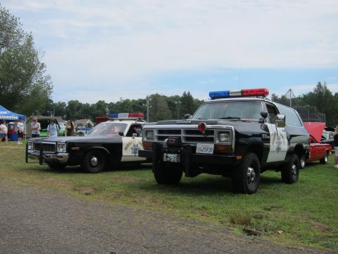 1991 Ford LTD Crown Victoria - black highway patrol sedan and a black-and-white Dodge Ramcharger displayed on grass at a car show.