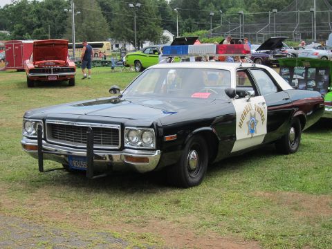 1991 Ford LTD Crown Victoria - black-and-white Highway Patrol sedan with push bar and roof light parked on grass at an outdoor car show.