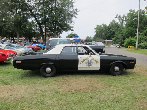 1991 Ford LTD Crown Victoria - Side profile of a black-and-white four-door Highway Patrol sedan with a single roof light, parked on grass at a car show.