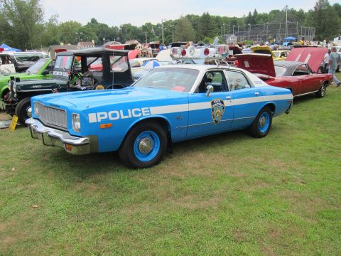 1991 Ford LTD Crown Victoria - two-tone blue-and-white sedan lettered POLICE with an NYPD shield and roof light, parked on grass among other show cars.