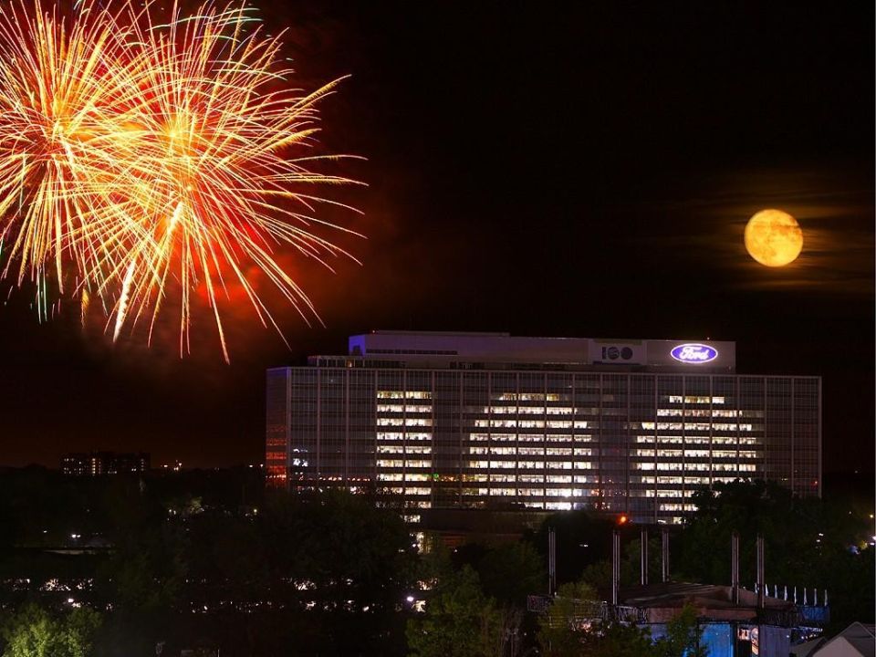 Ford headquarters building at night with 100th anniversary sign, fireworks and full moon