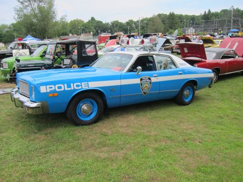 1991 Ford LTD Crown Victoria - Side profile of a blue-and-white four-door police sedan with POLICE lettering and an NYPD shield, parked on grass at an outdoor car show.