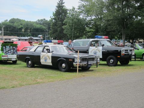 1991 Ford LTD Crown Victoria - black-and-white Highway Patrol sedan parked beside a matching patrol SUV with light bars, on grass at an outdoor car show.