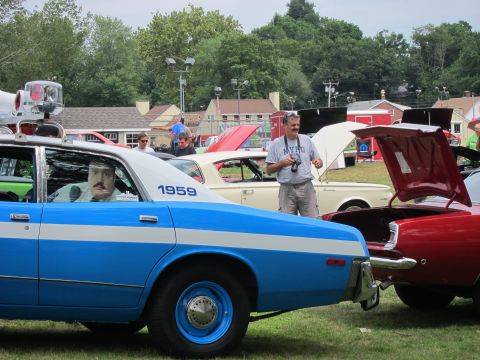 1991 Ford LTD Crown Victoria - Rear quarter of a blue-and-white police sedan marked 1959 with a uniformed mannequin in the window, beside a red car at a show.