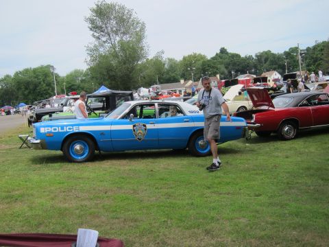 1991 Ford LTD Crown Victoria - Side profile of a blue-and-white NYPD POLICE sedan marked 1959 parked on grass, with a man walking past at a busy car show.