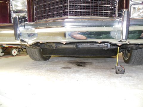 1979 Ford Ranchero - Low ground-level view of the front of a burgundy car in a garage, framing the polished chrome bumper with its guards, the black eggcrate gr…