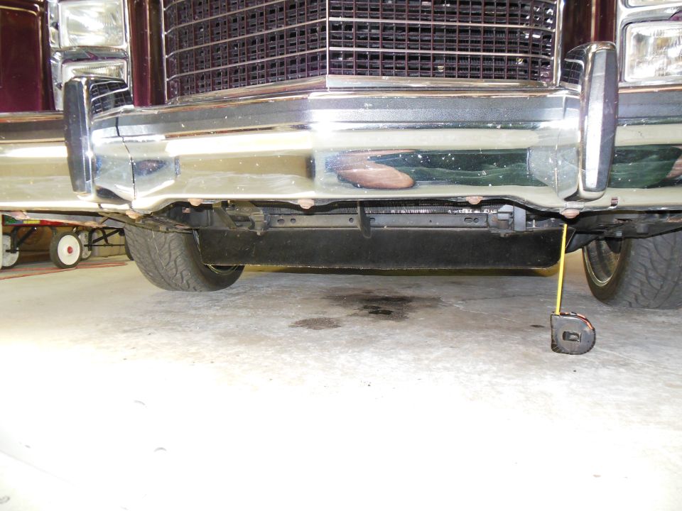 Low front view of burgundy car's chrome bumper and valance with tape measure to floor