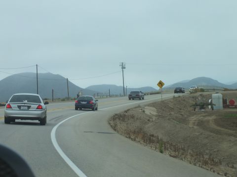 2003 Ford Crown Victoria - Through a windshield, a silver sedan leads dark sedans around a highway bend toward foggy hills.
