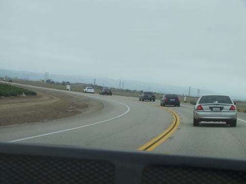 2003 Ford Crown Victoria - From inside a car, a silver sedan trails dark sedans along a double-yellow highway beside hills.