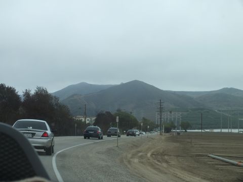 2003 Ford Crown Victoria - Through a windshield, a silver sedan and dark cars travel a highway beneath tall fog-shrouded peaks.