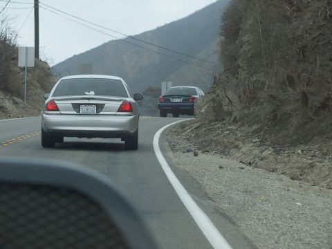 2003 Ford Crown Victoria - silver sedan follows a black sedan around a bend on a winding two-lane mountain road.