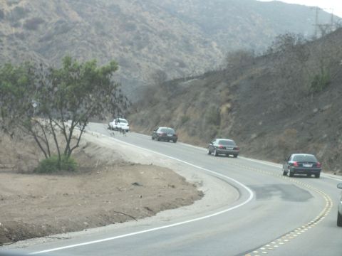 2003 Ford Crown Victoria - string of sedans winds along a two-lane road cutting through dry brush-covered hillsides.