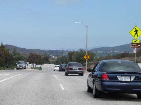 2003 Ford Crown Victoria - dark blue Ford sedan with a 'BLUE VIC' license plate drives a road past a yellow crossing sign and a National/State Parks marker.