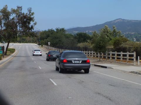 2003 Ford Crown Victoria - gray full-size sedan and a dark sedan travel a road bordered by a wooden ranch fence with mountains in the distance.