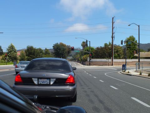 2003 Ford Crown Victoria - gray Ford full-size sedan with plate 5YWN854 waits at a red light at a wide intersection with overhead signals and hills beyond.