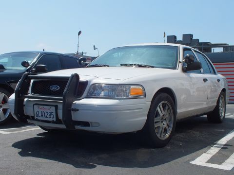 2003 Ford Crown Victoria - Front three-quarter view of a white Ford sedan with a black push bumper and California plate 6LAX285.
