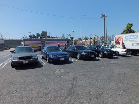 2003 Ford Crown Victoria - row of sedans including a gray and a blue Ford parked next to a white Hill-Rom box truck under a clear sky.
