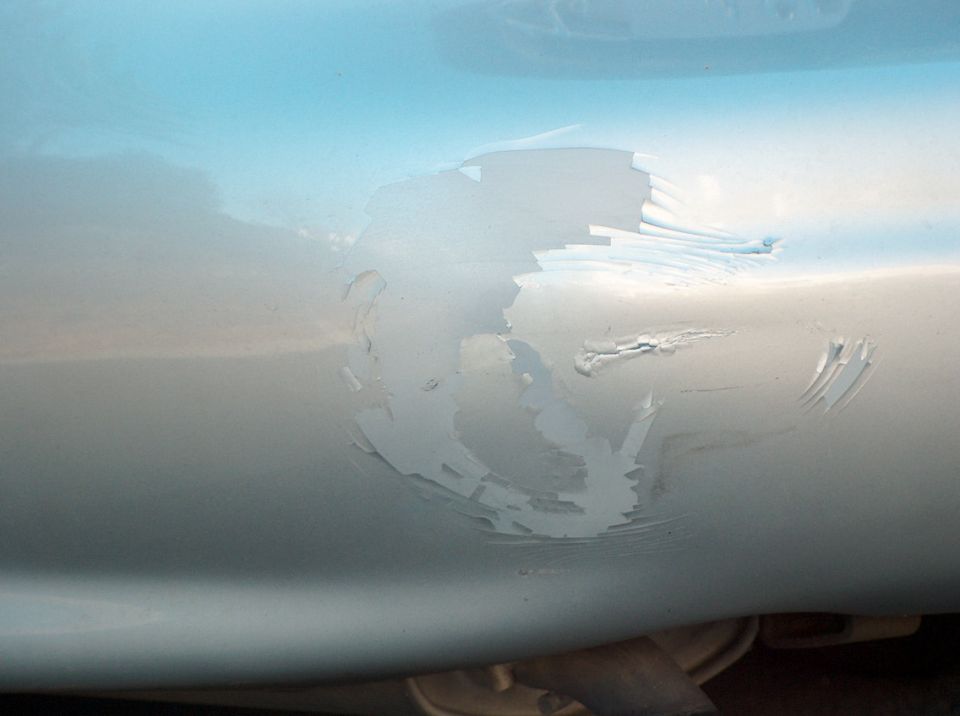 Close-up of peeling paint and scratches on a light blue car body