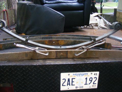 1978 Ford Bronco - Leaf springs are shown clamped to wooden blocks on a trailer, with a black leather armchair visible behind them.